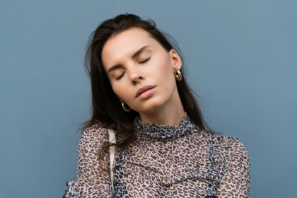 Beautiful woman in leopard fitting dress with white bag posing on blue wall background