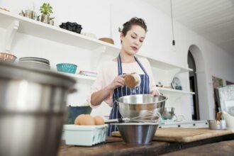 Young woman pouring flour into bowl at kitchen counter